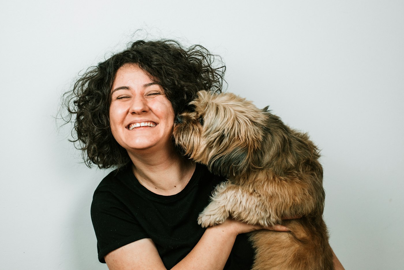 A woman laughing as a small terrier licks her cheek